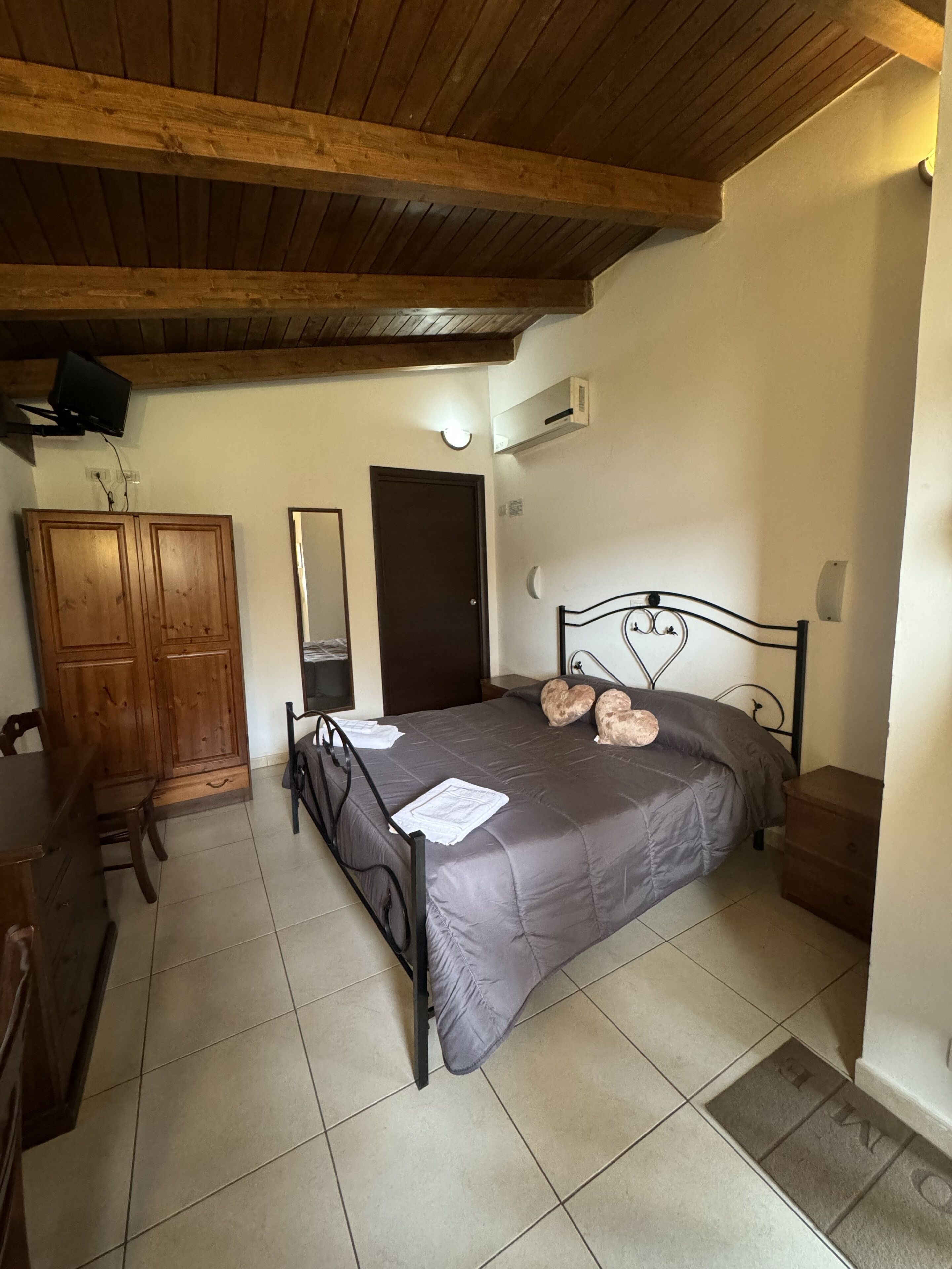 Ein Schlafzimmer mit Bett, Holzschrank, Spiegel und Tür.