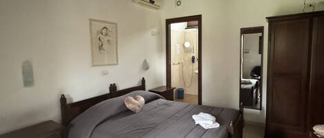 A bedroom with a wooden ceiling, a bed with a grey bedspread, a nightstand, a dresser, and a mirror.