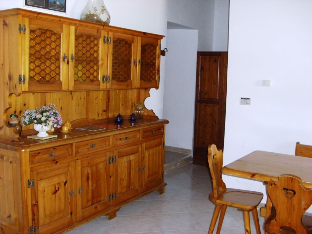 A wooden dining table with chairs, a wooden cabinet with drawers, and a vase with flowers on the cabinet.