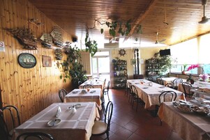 Un restaurante con paredes de madera, varias mesas, sillas y plantas colgantes.