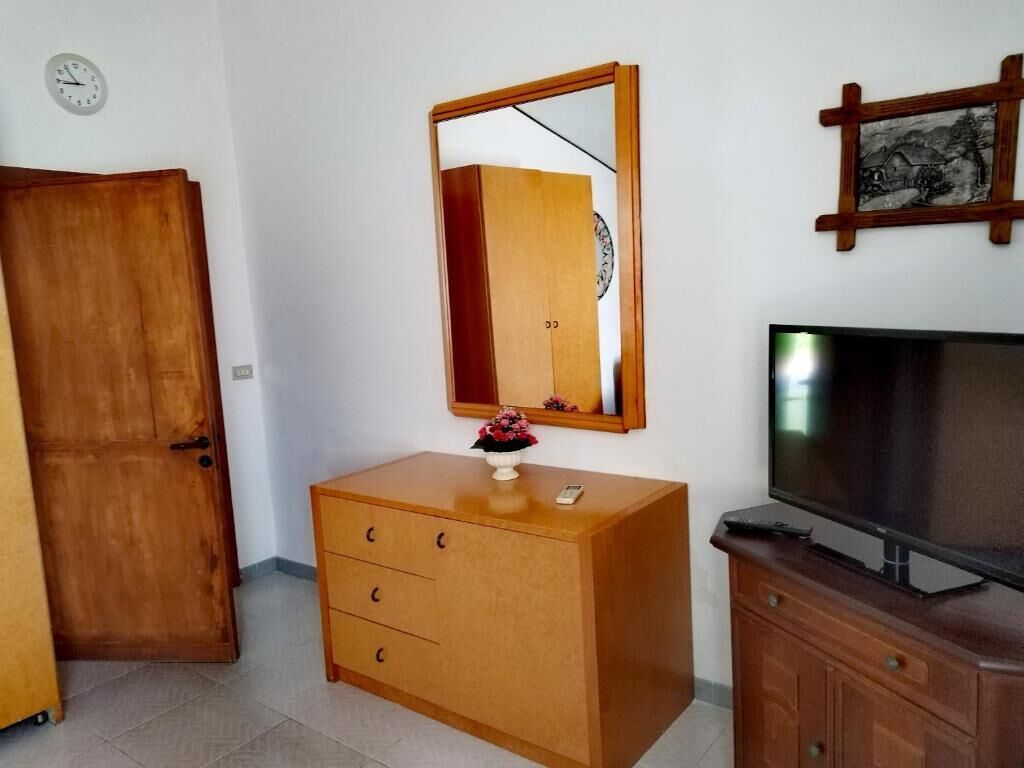 A room with a wooden wardrobe, a mirror, a television, and a clock on the wall.