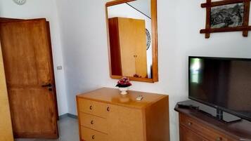 A room with a wooden wardrobe, a mirror, a television, and a clock on the wall.