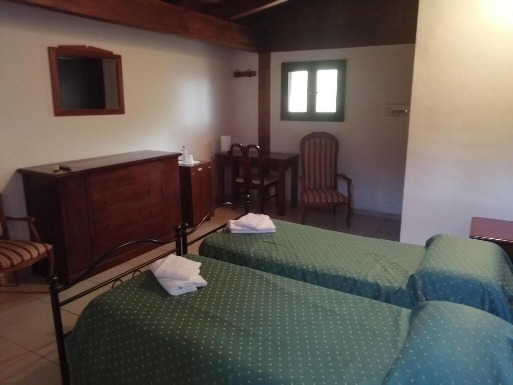A room with two beds, a wooden dresser, a chair, a small table, and a window.