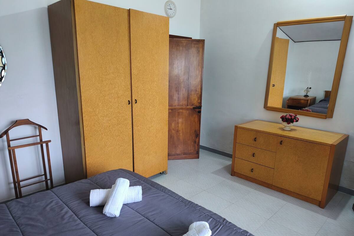A bedroom with a bed, a wardrobe, a dresser, a mirror, and a clock on the wall.