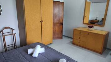 Una camera da letto con un letto, un armadio, una cassettiera, uno specchio e una sveglia appesa al muro.