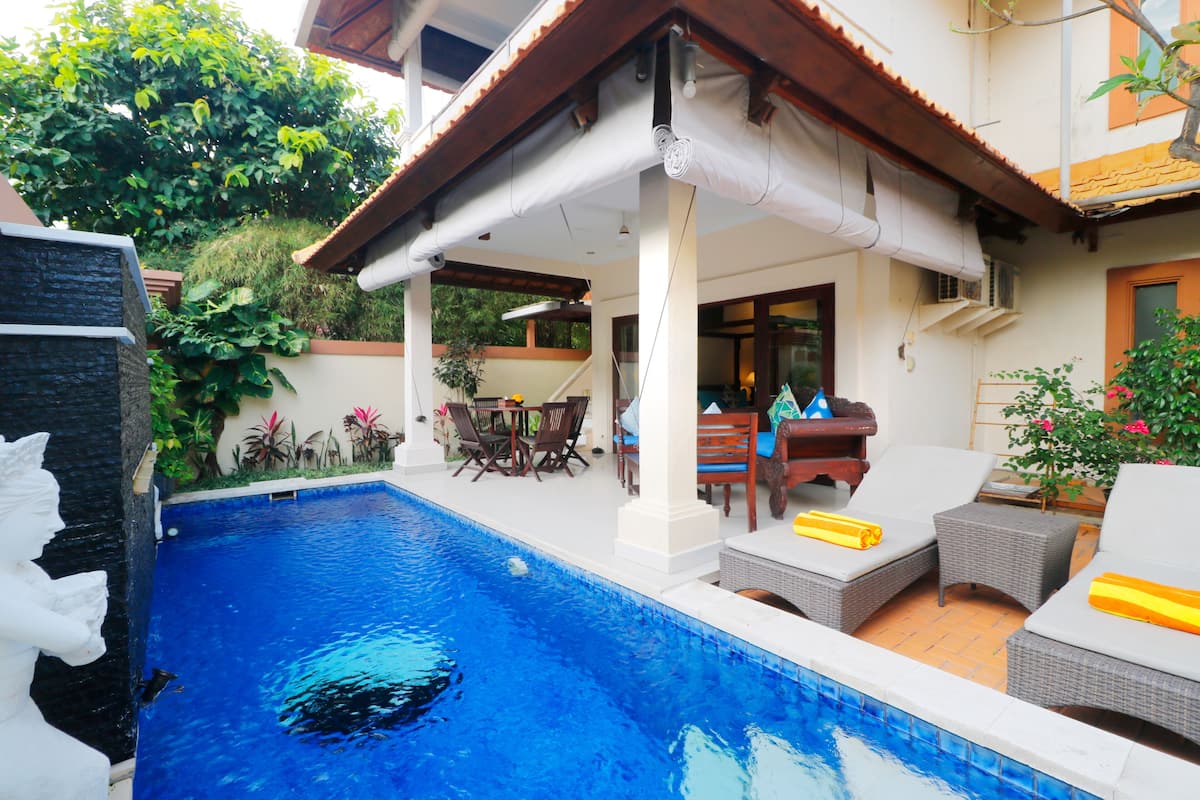 Un área junto a la piscina con una piscina azul cristalina, mobiliario exterior y una zona de estar cubierta.
