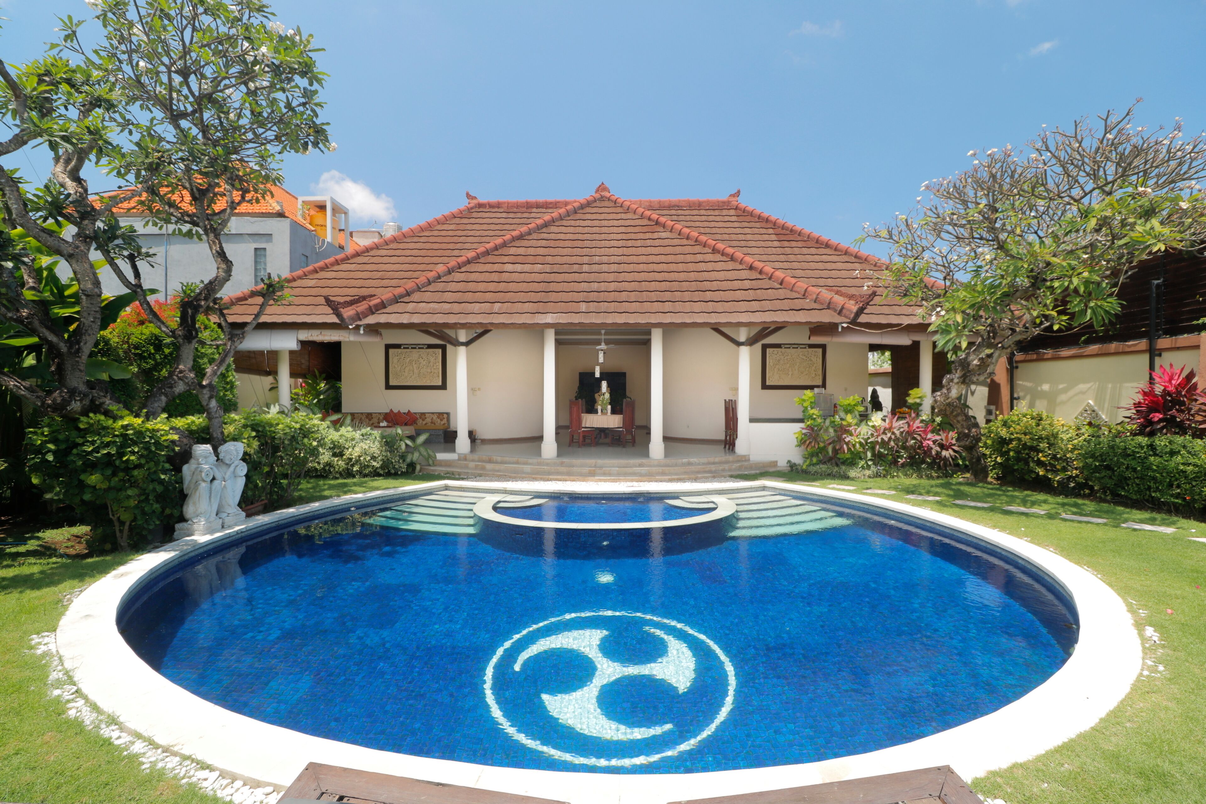 A house with a swimming pool in front, a tiled roof, and a statue.