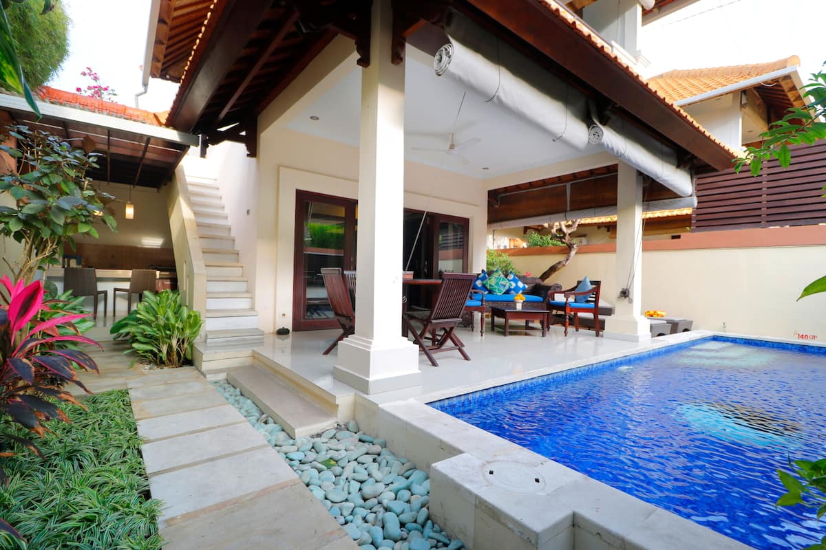 Una piscina con borde de piedra, rodeada por un patio con mobiliario exterior y plantas.