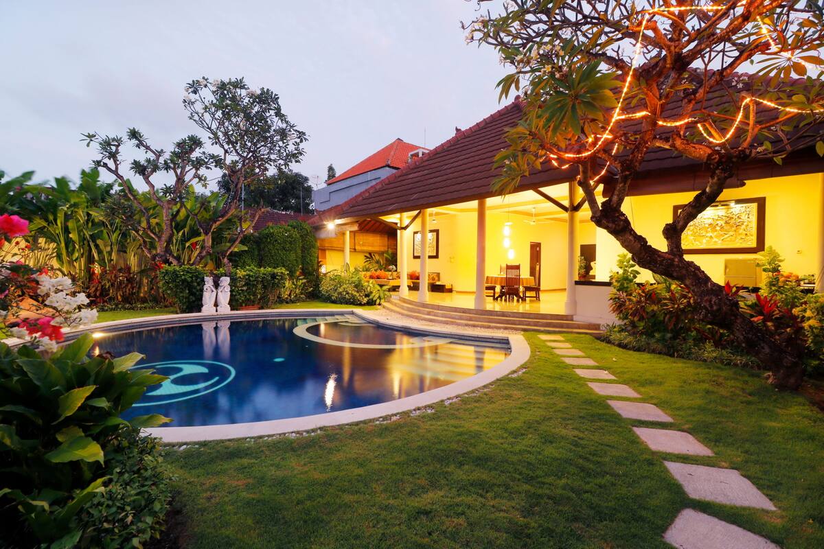 Un jardín bien cuidado con una piscina, un patio y una casa con techo de tejas.