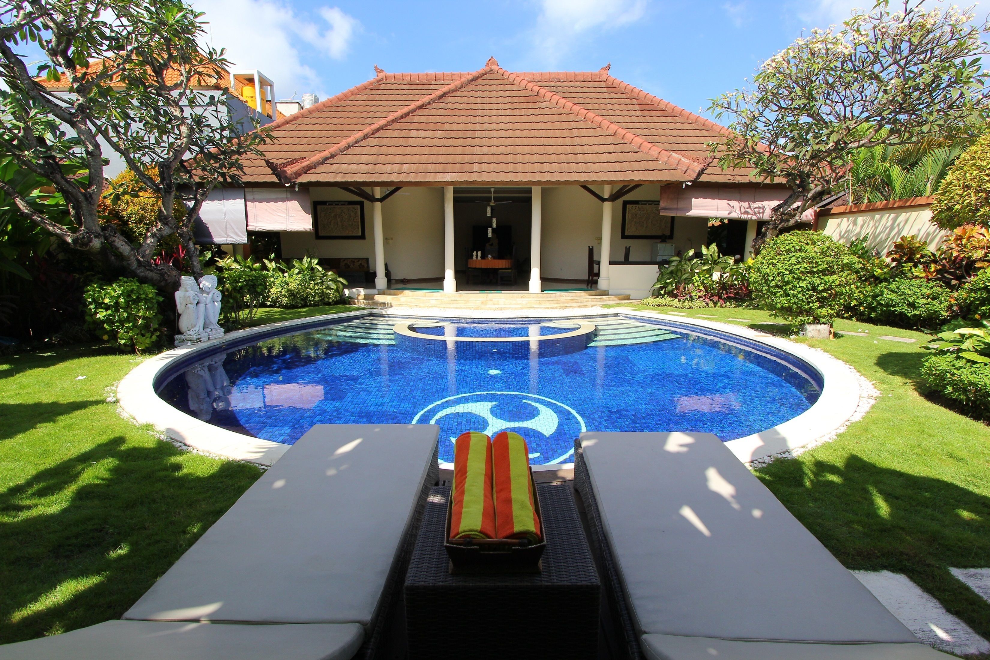A swimming pool with a tiled roof, surrounded by a well-maintained lawn and various plants.