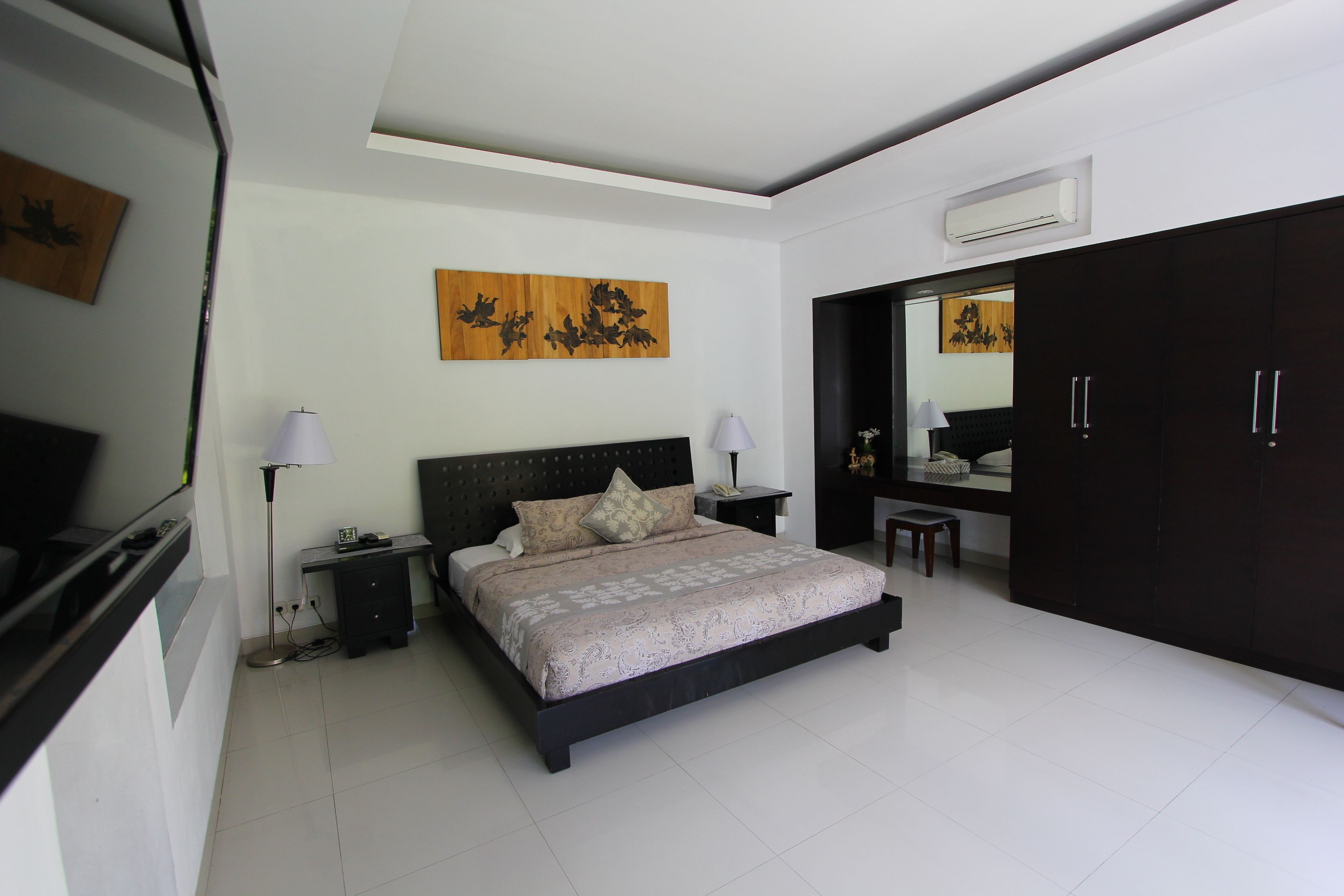 A modern bedroom with a large bed, bedside lamps, a desk, and a wardrobe.