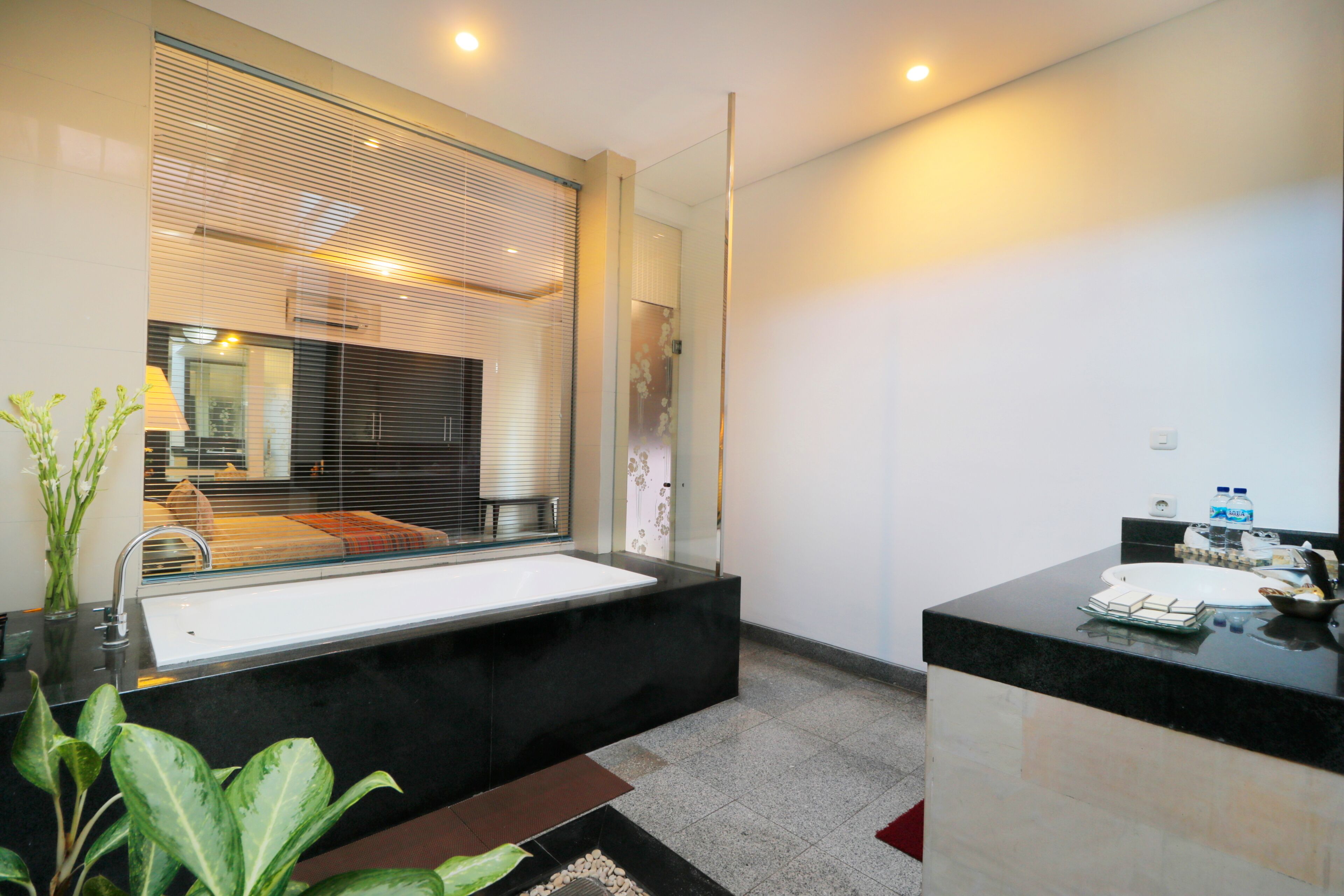 Un baño moderno con un espejo grande, una encimera negra y una zona de ducha con mampara de cristal.
