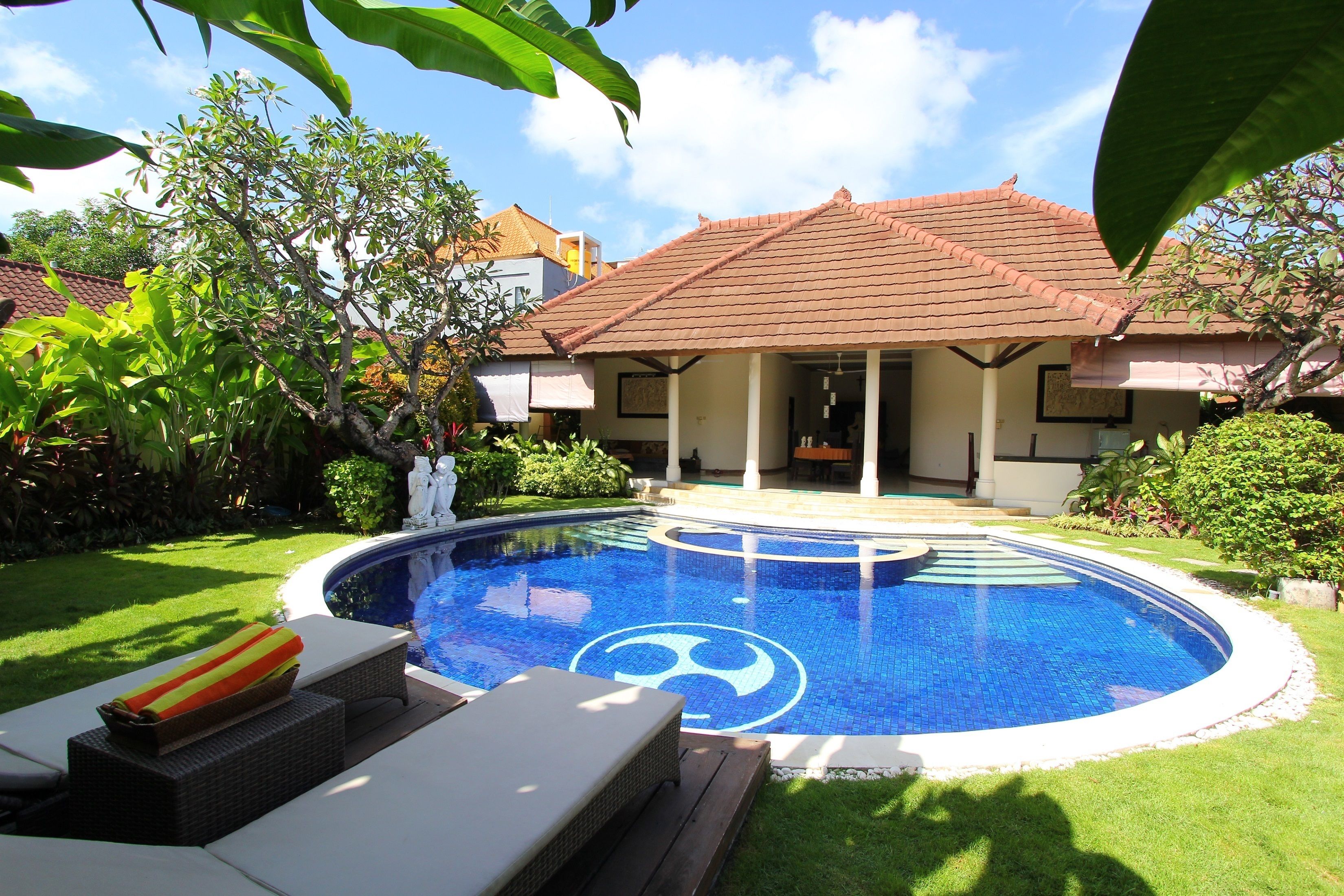 A swimming pool with a tiled design, surrounded by a well-maintained lawn and a house with a tiled roof.