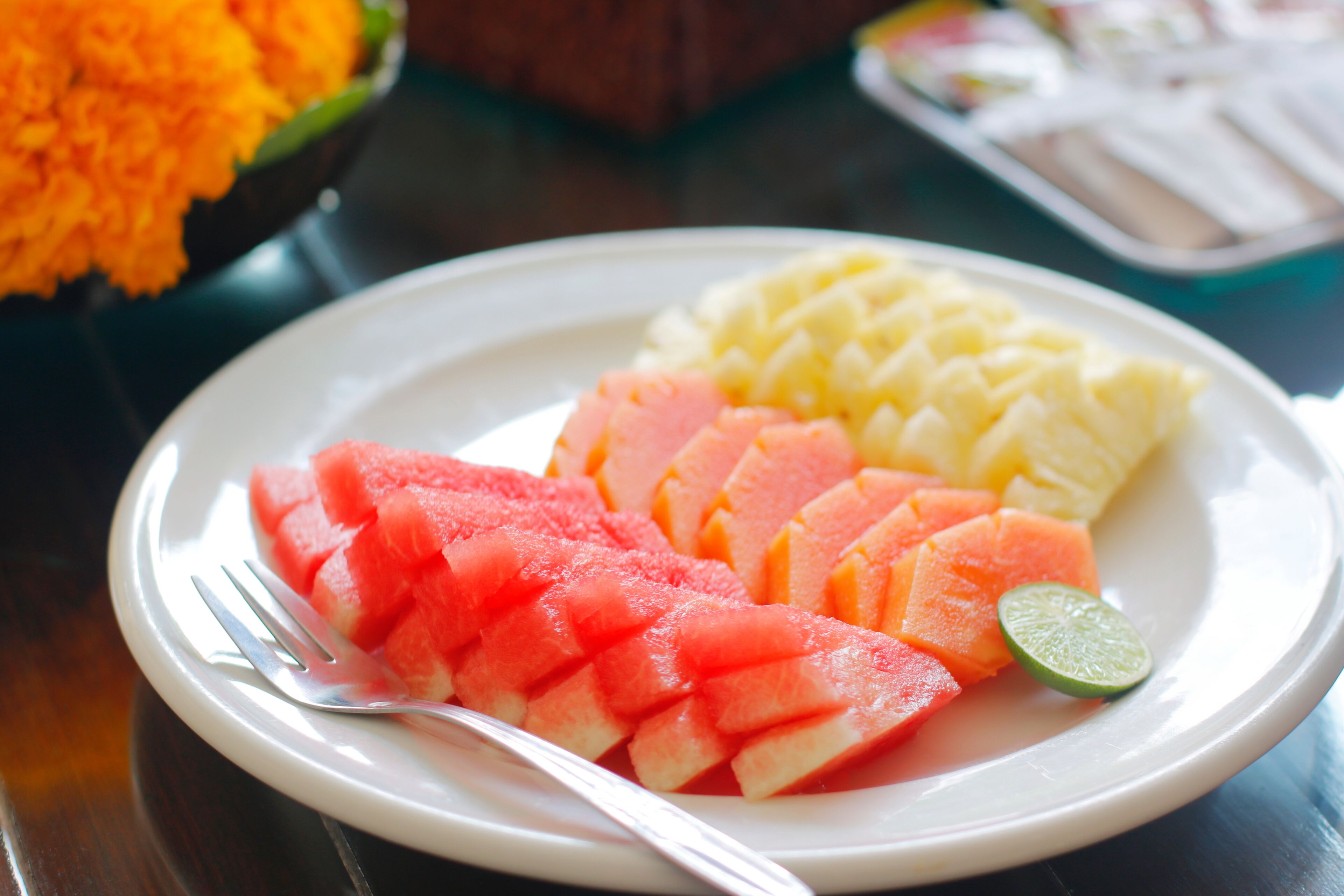 A plate with sliced watermelon, pineapple, and a lime wedge.
