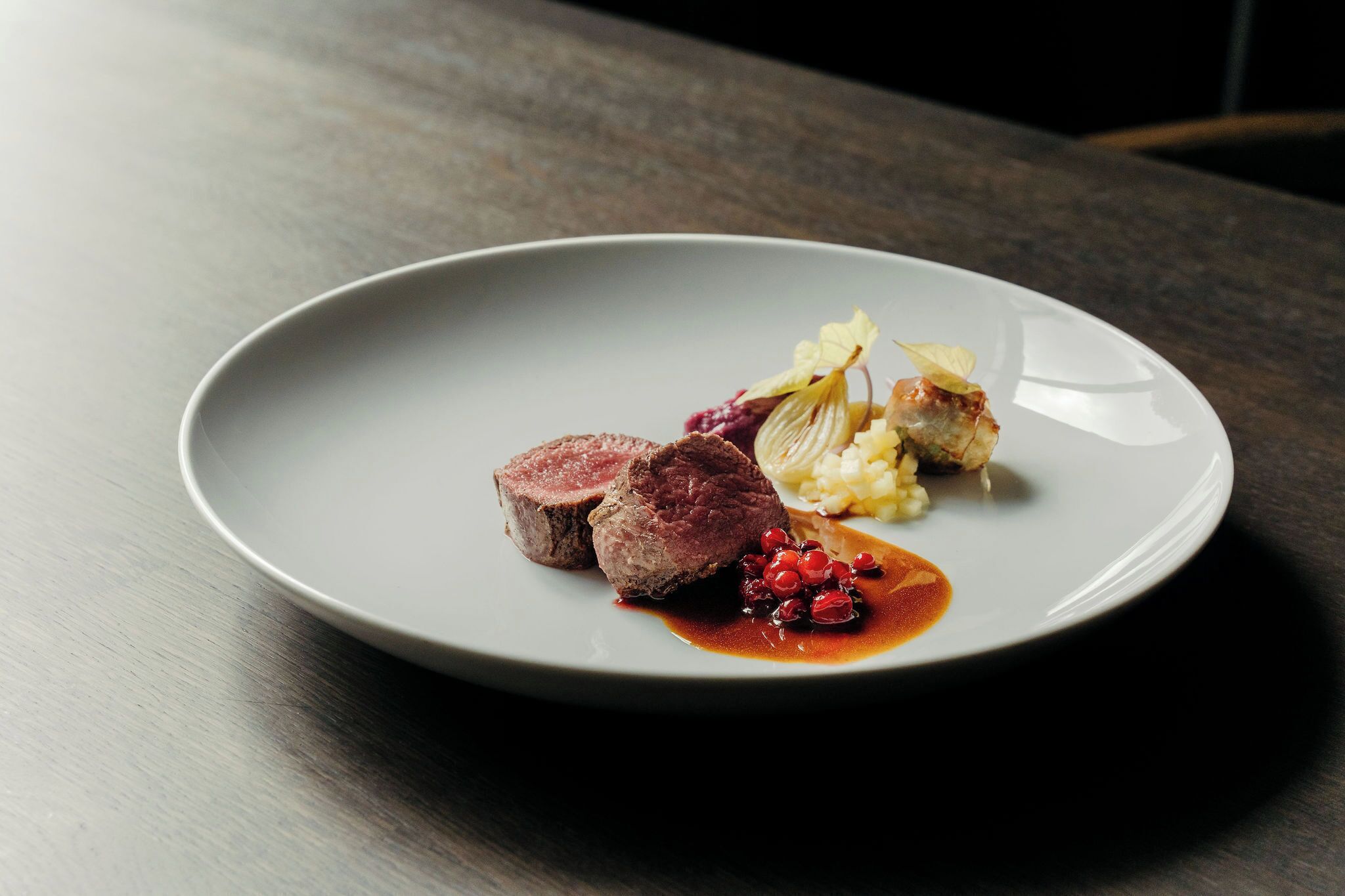 A plate with a piece of meat, a small portion of mashed potatoes, and a garnish of berries and leaves.