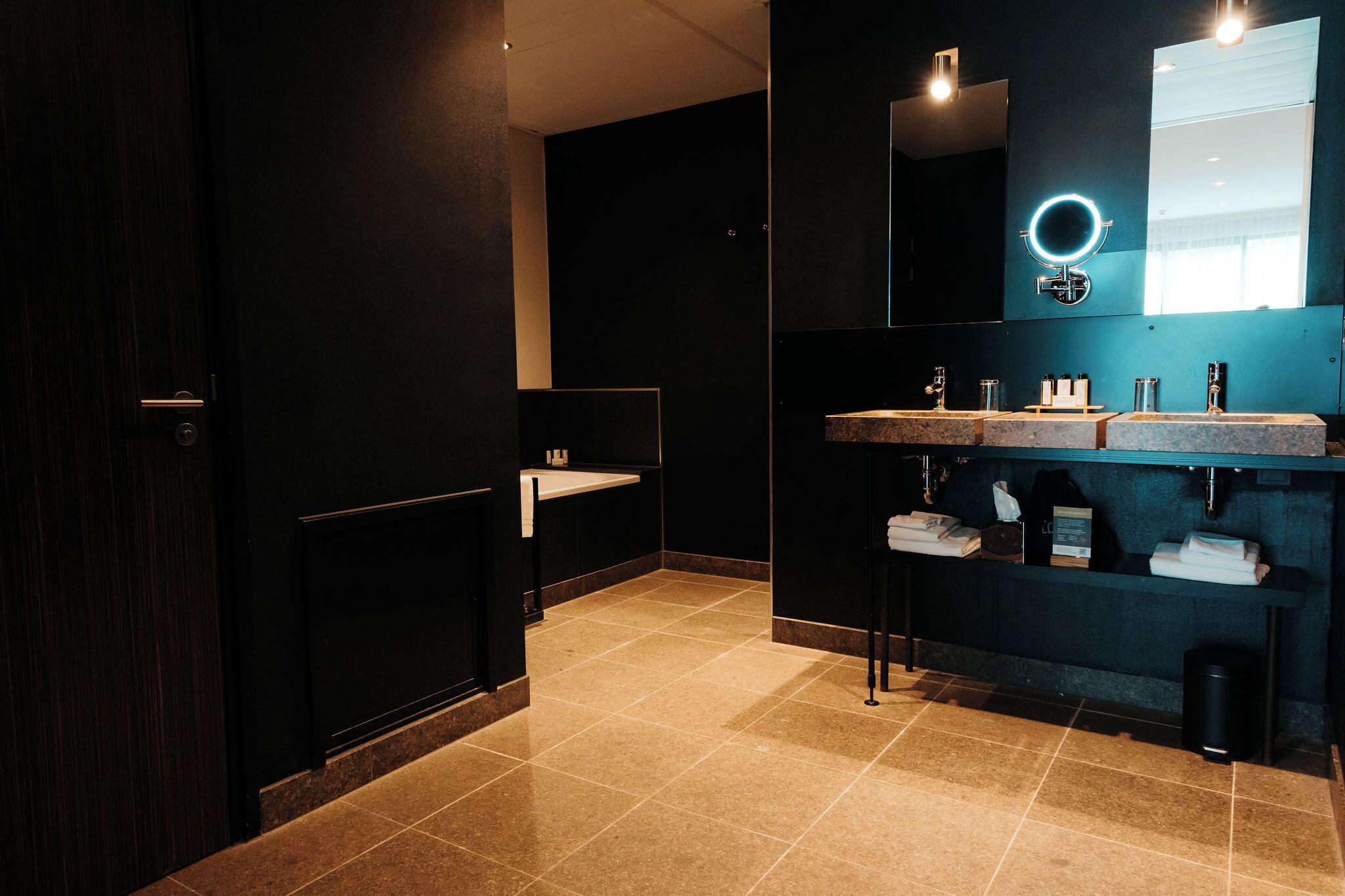Un baño moderno con paredes oscuras, un espejo grande y dos lavamanos.
