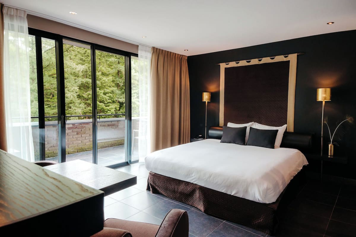 Een moderne hotelkamer met een groot bed, een bureau en uitzicht op een balkon met glazen deuren.