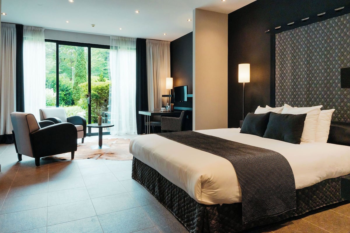 Een moderne hotelkamer met een groot bed, een bureau en een stoel. Er is een televisie aan de muur en een raam met gordijnen.