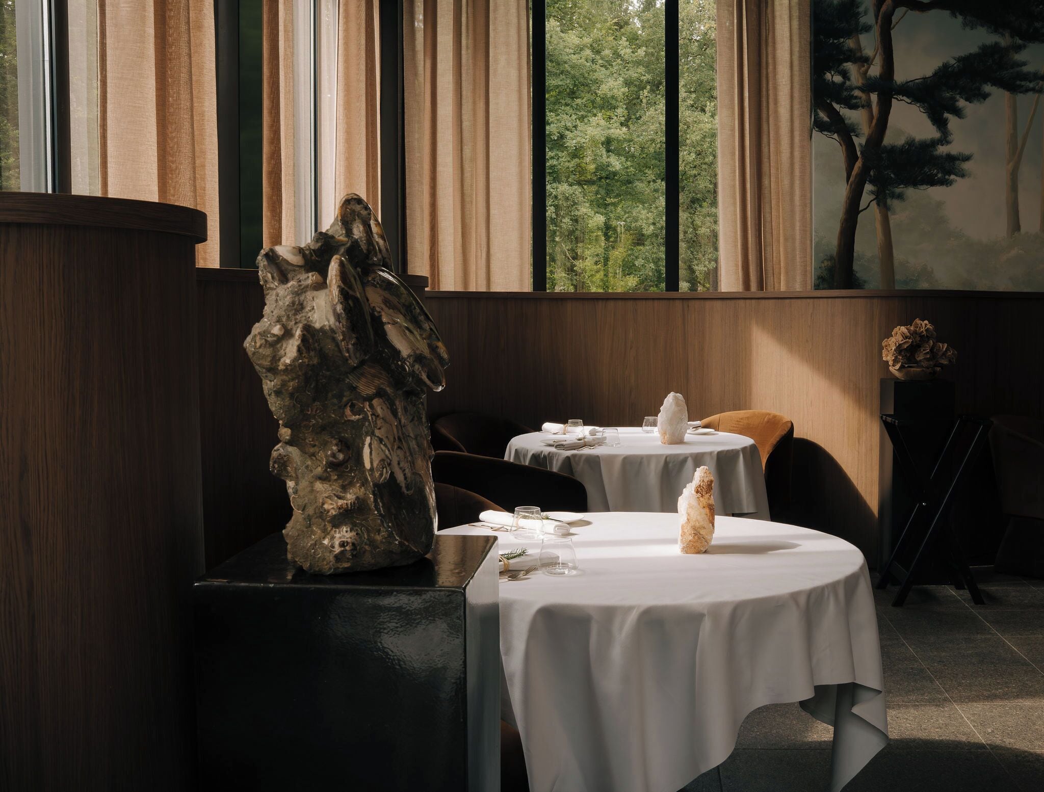 A dining area with round tables, white tablecloths, and a large wooden sculpture.