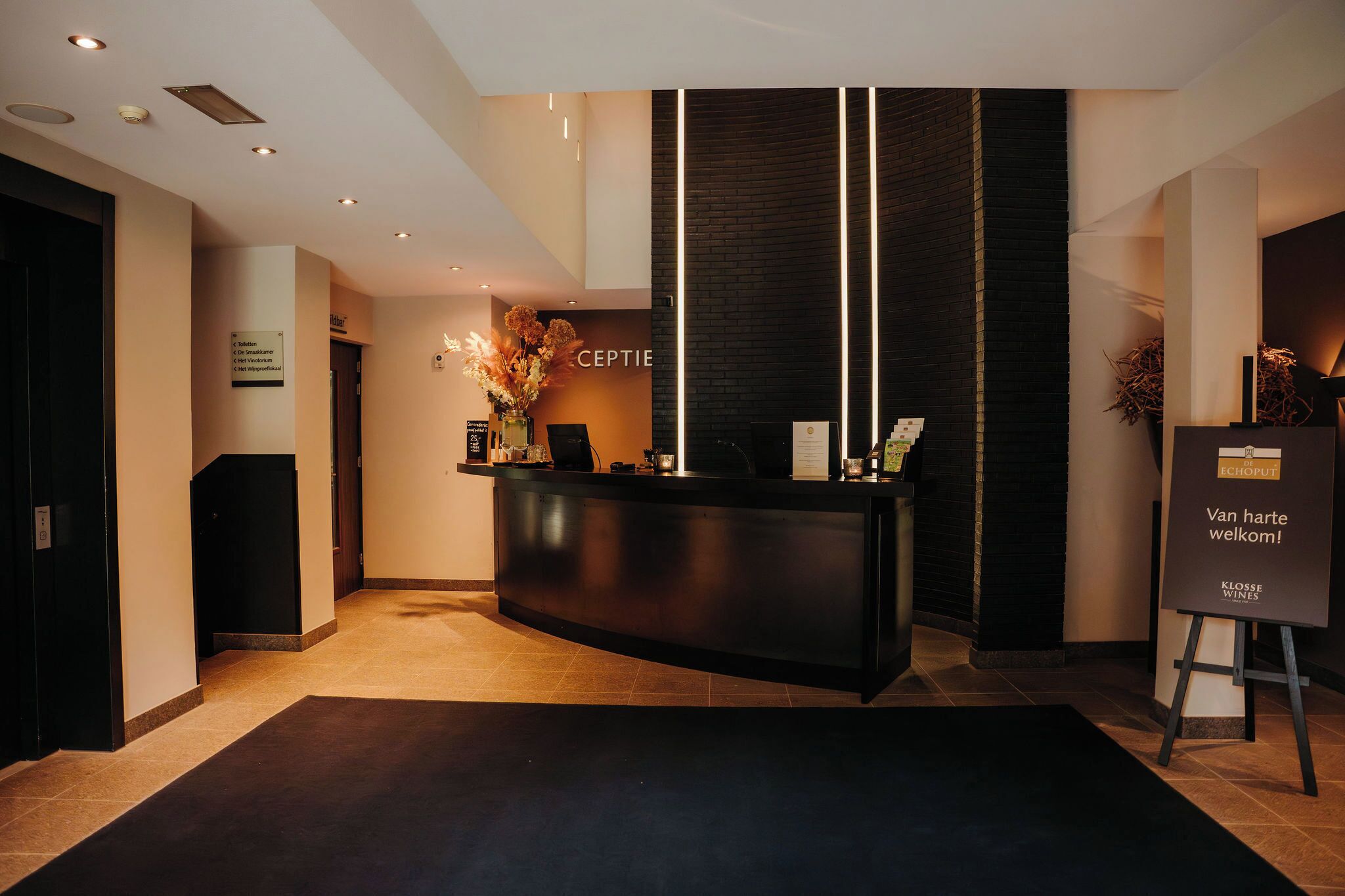 A reception area with a black reception desk, a sign reading "RECEPTION," and a welcome sign for "KLOSSE WINES."