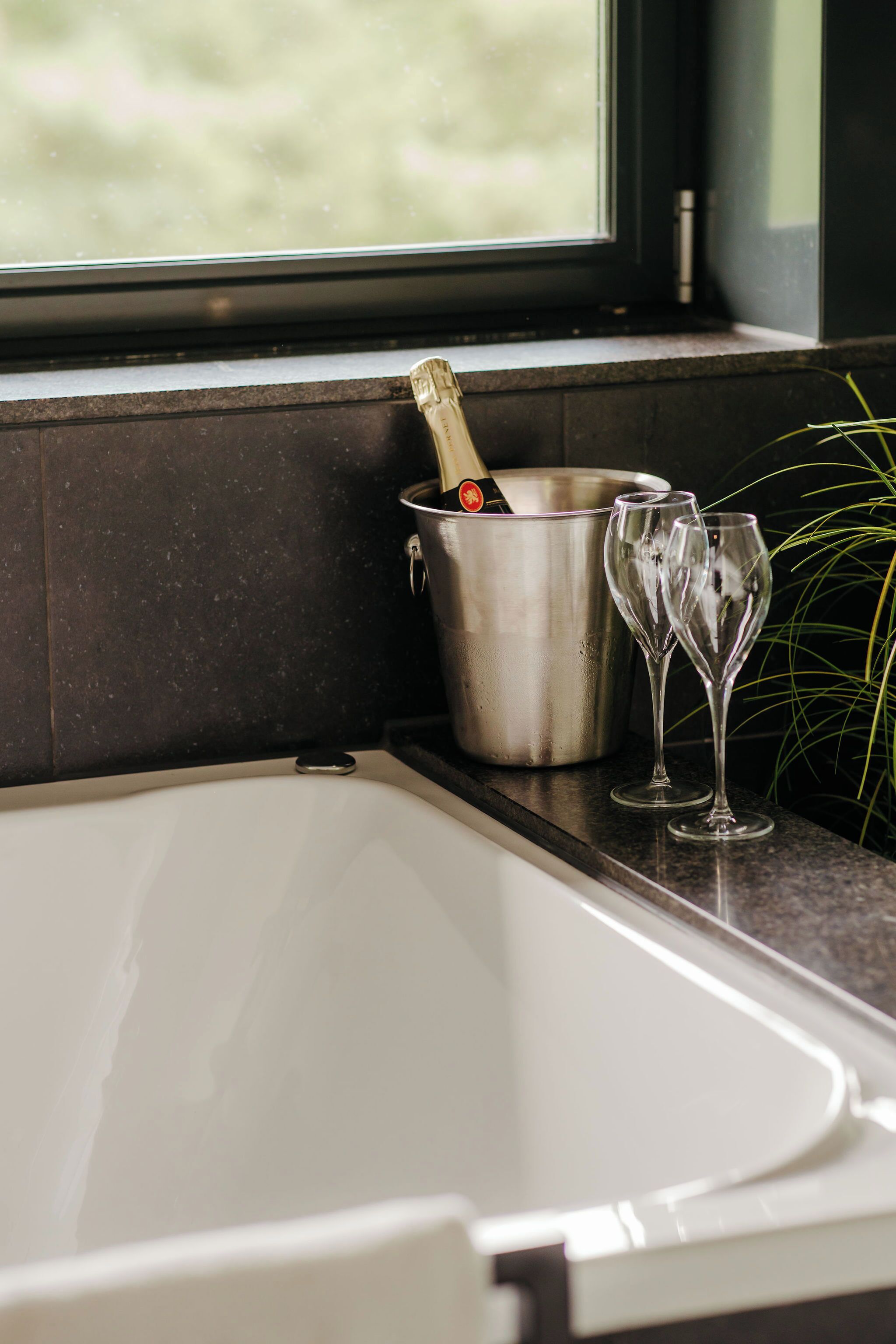 A modern bathroom with a bathtub, a champagne bottle in a bucket, and two champagne flutes on the counter.