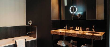 A modern bathroom with a bathtub, two sinks, a vanity, and a large mirror with a light.