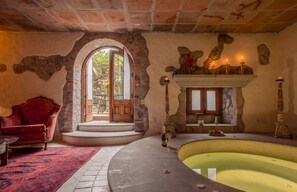 Una habitación con chimenea de piedra, un sillón rojo, una piscina y una vista a través de una puerta.