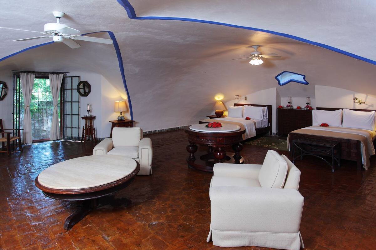 Una habitación acogedora con una mesa redonda, dos sillones blancos, una cama y un ventilador de techo.