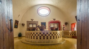 Una habitación circular con suelo de baldosas, una plataforma central elevada con diseño de cuadros y un tragaluz superior.