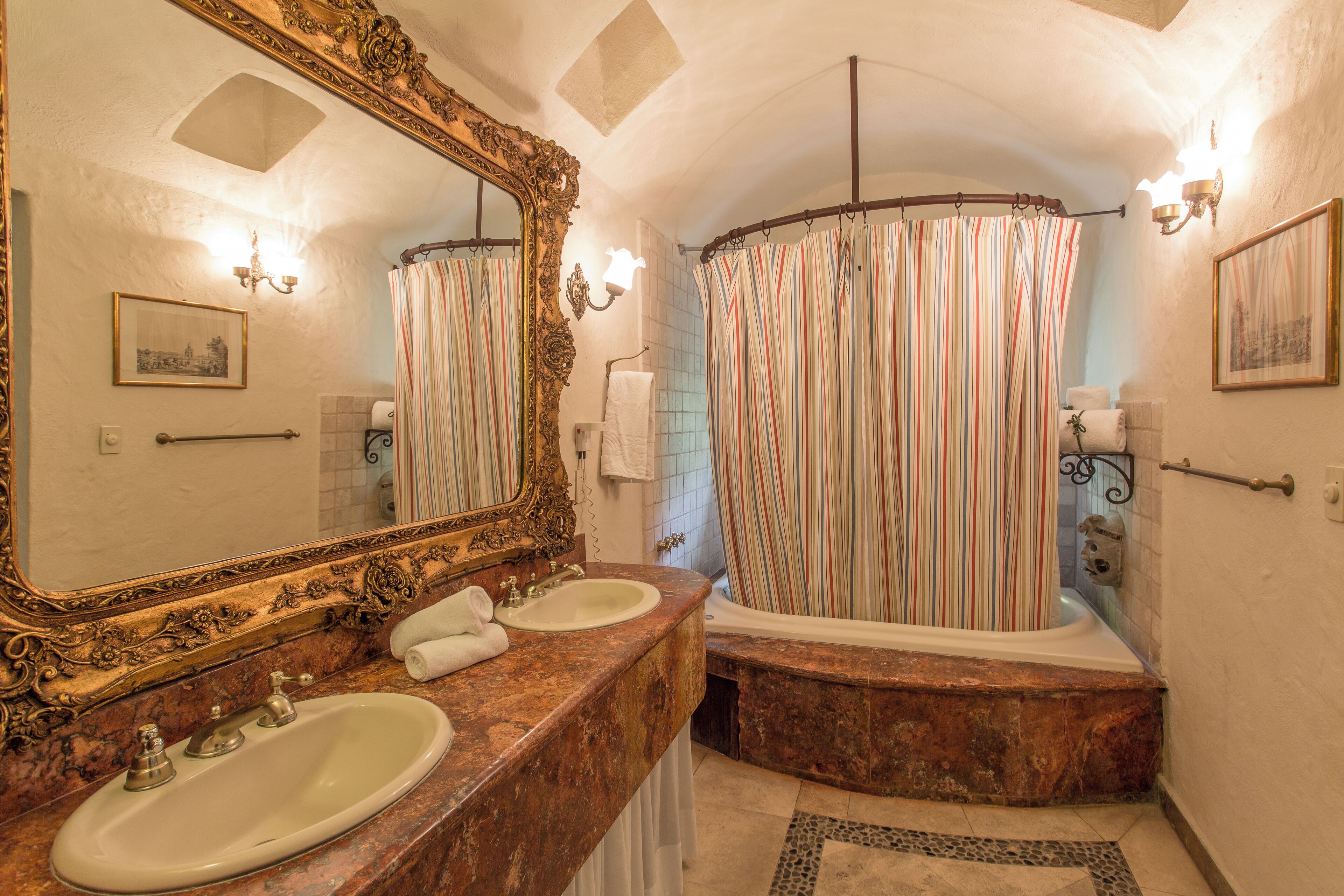 A bathroom with two sinks, a bathtub, a shower curtain, and a large ornate mirror.