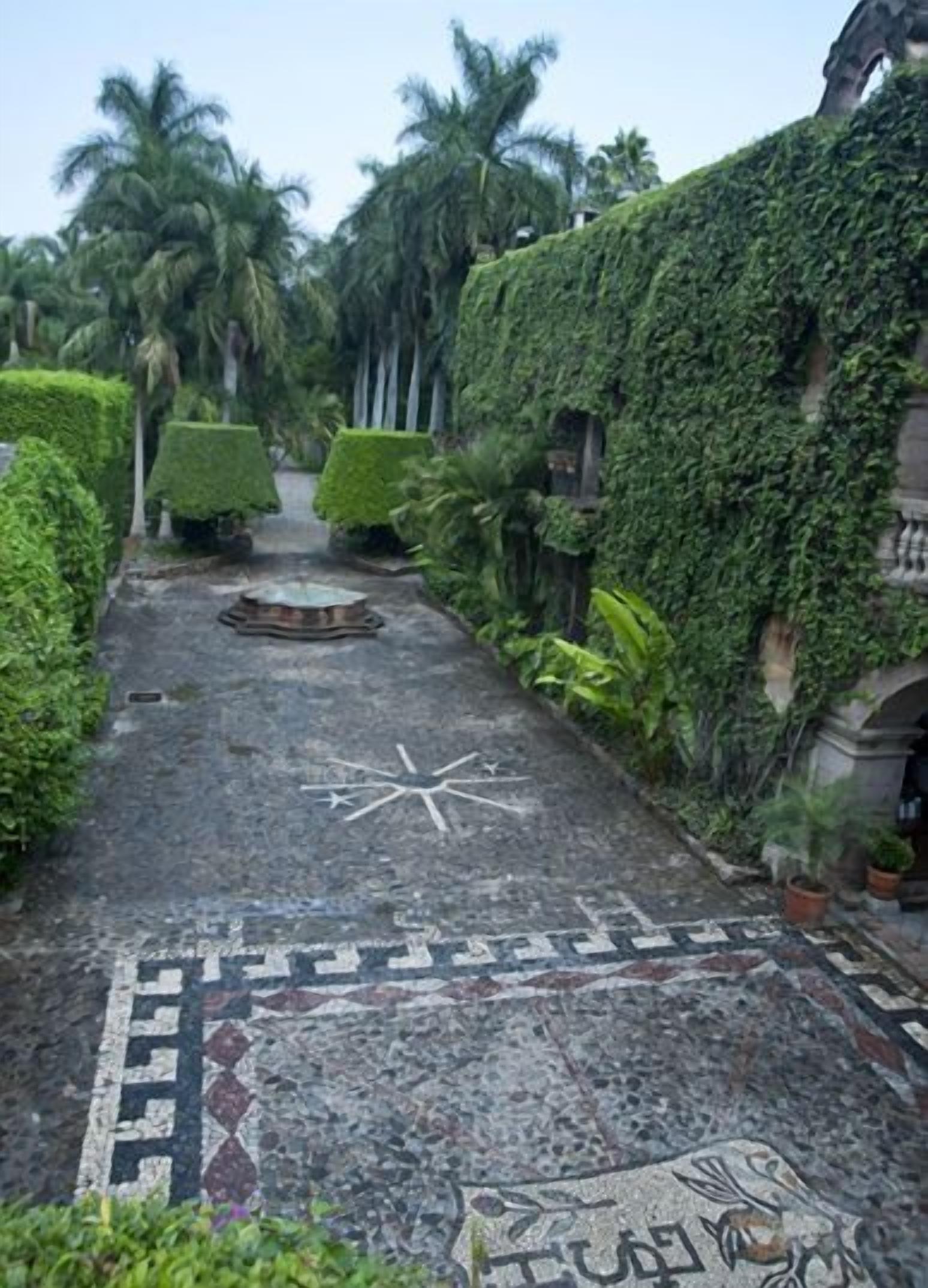 Un sendero pavimentado con un mosaico en forma de estrella, rodeado de exuberante follaje y palmeras.