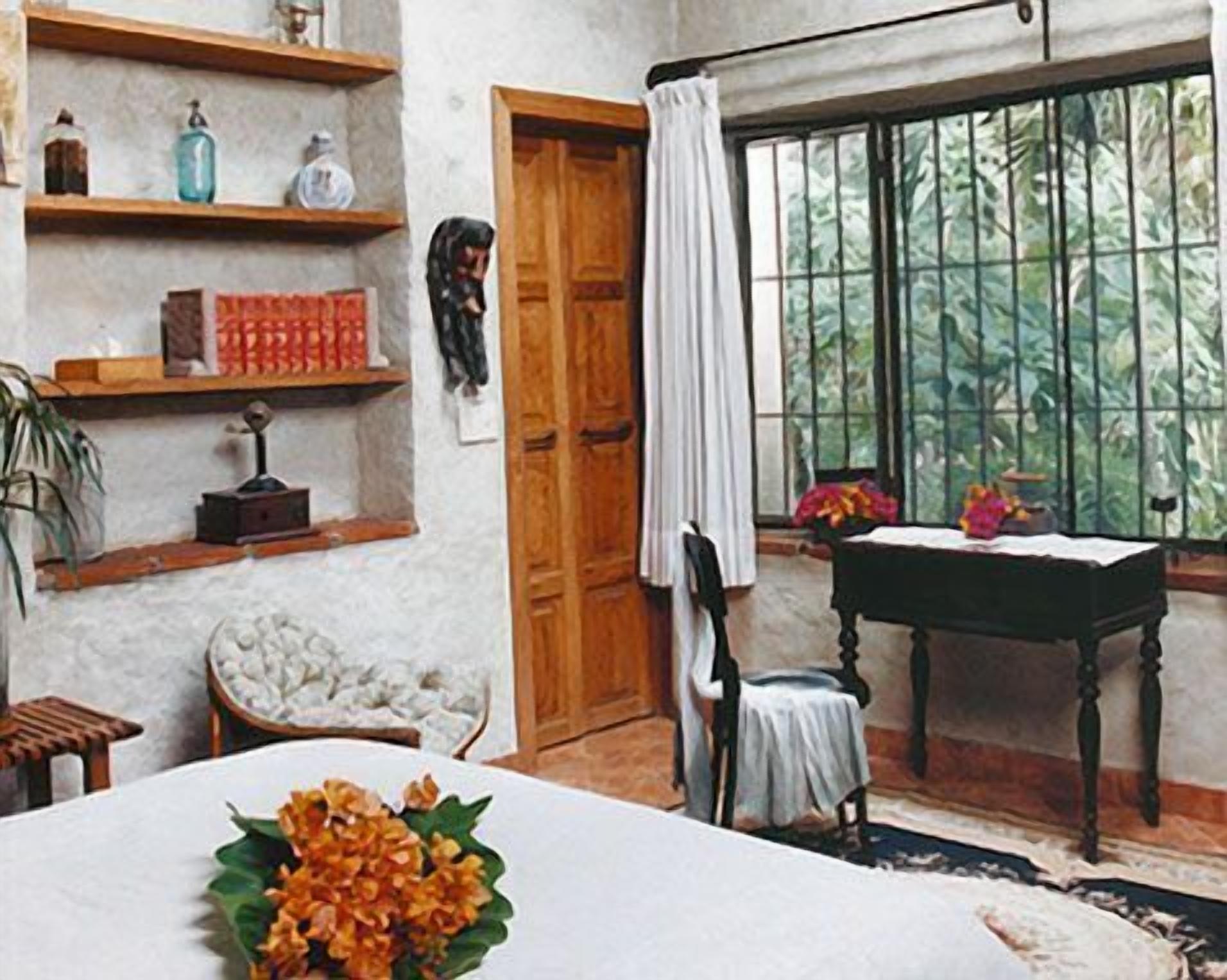 A room with a wooden door, a window with bars, a table with a chair, and a shelf with various items.