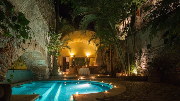 Une piscine intérieure avec un mur en pierre et des plantes tropicales, entourée d’un chemin en pierre.