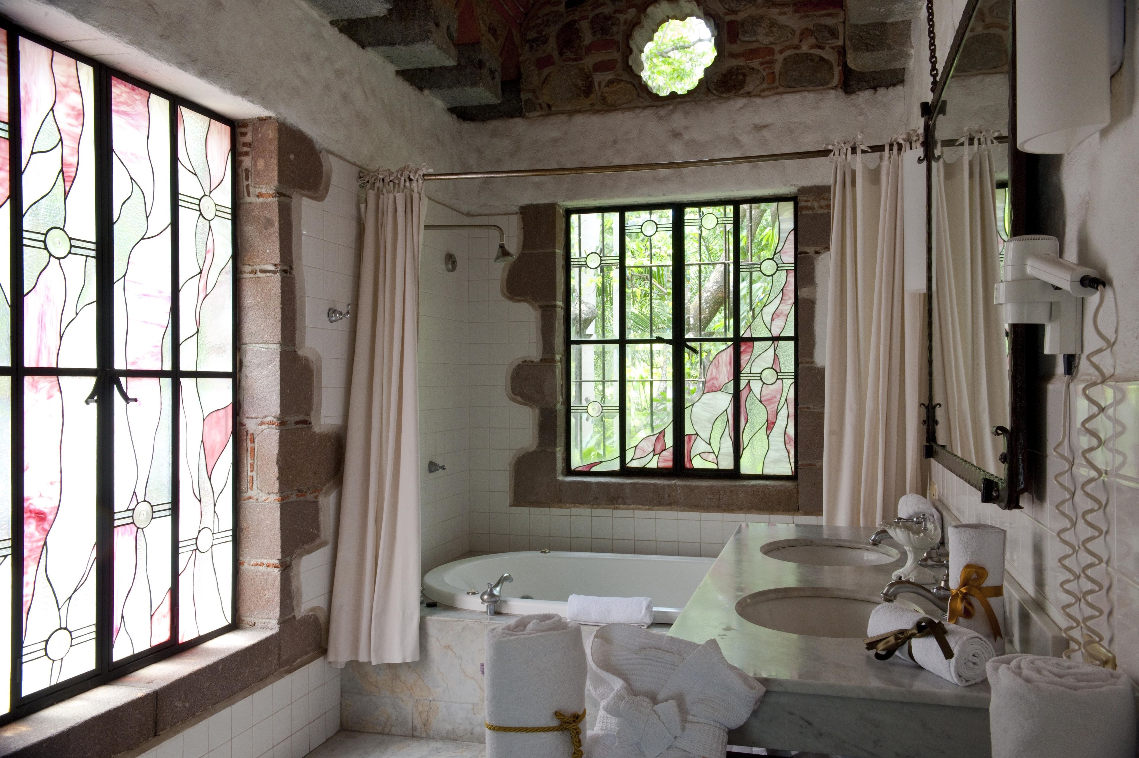 A bathroom with a bathtub, two sinks, and a large window with stained glass.