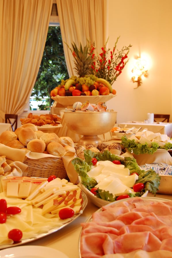 A buffet table with various food items including breads, cheeses, meats, and fruits.