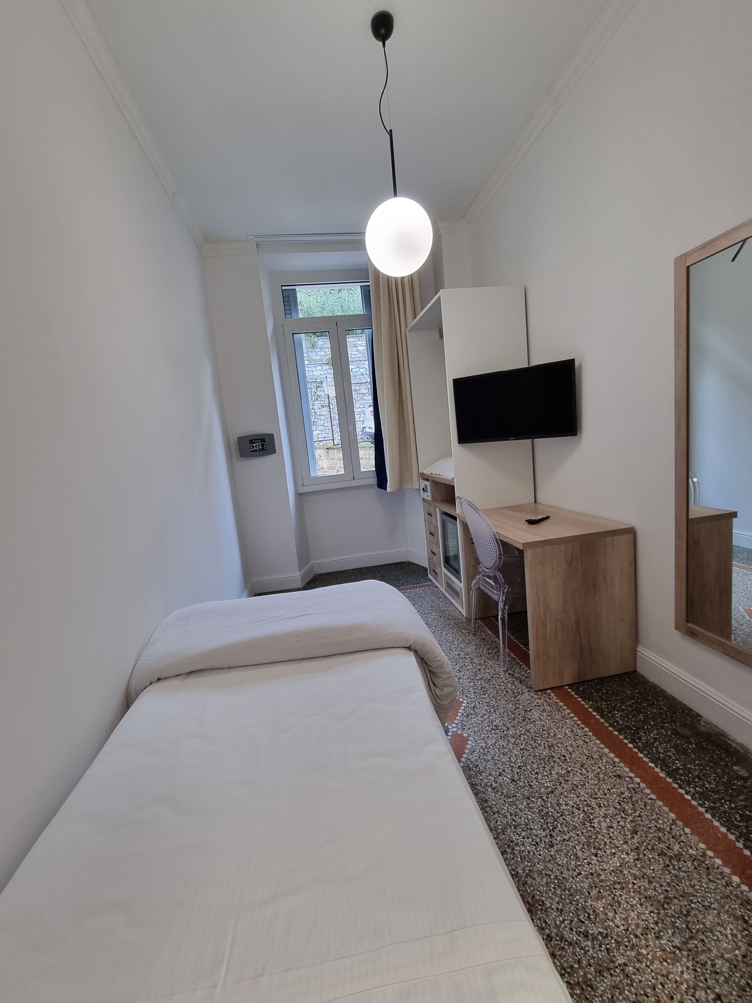 Een slaapkamer met een bed, een bureau met een televisie, een raam en een spiegel.