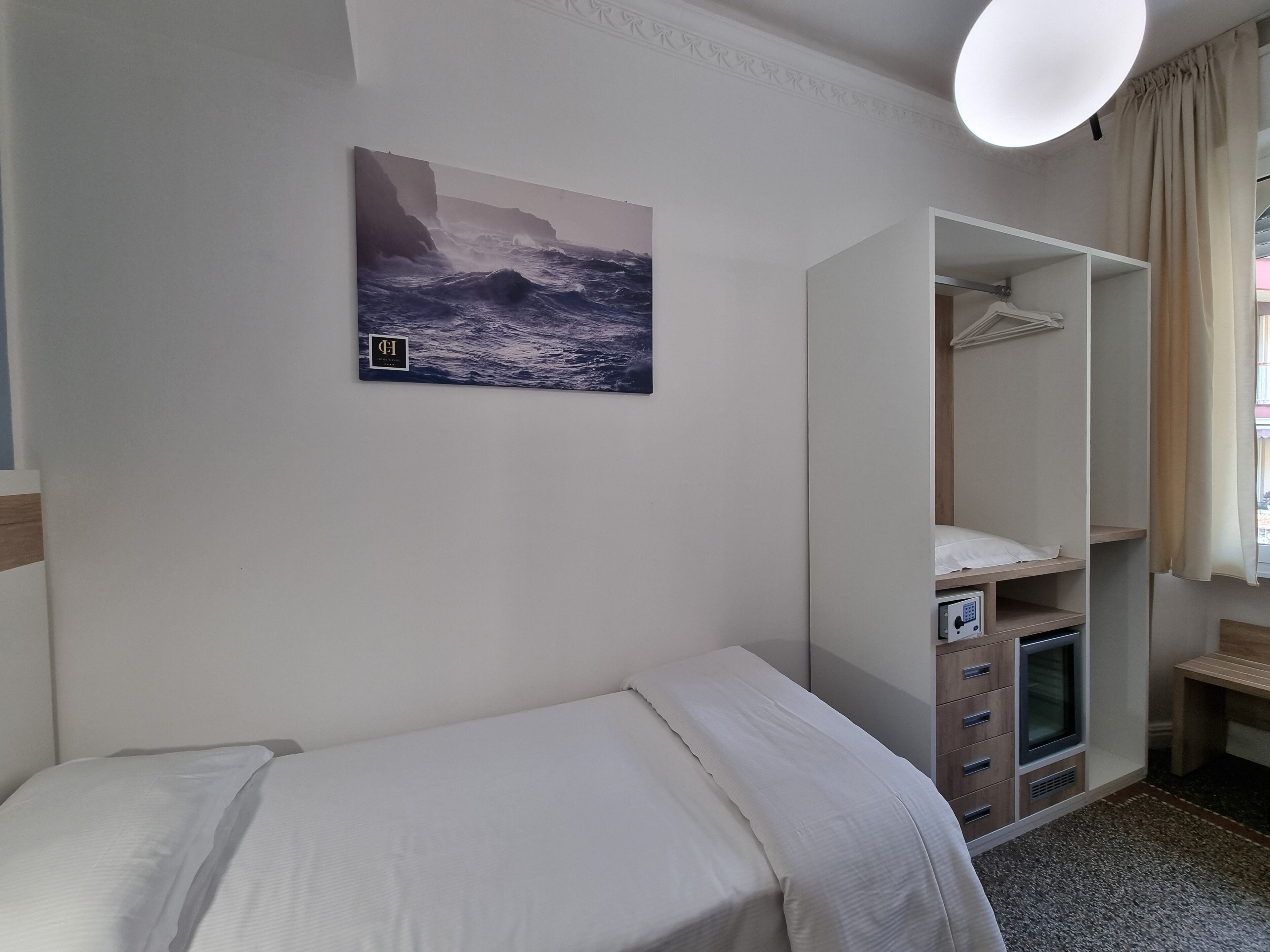 Une chambre d’hôtel avec un lit, une armoire, un téléviseur et un tableau représentant un paysage marin.