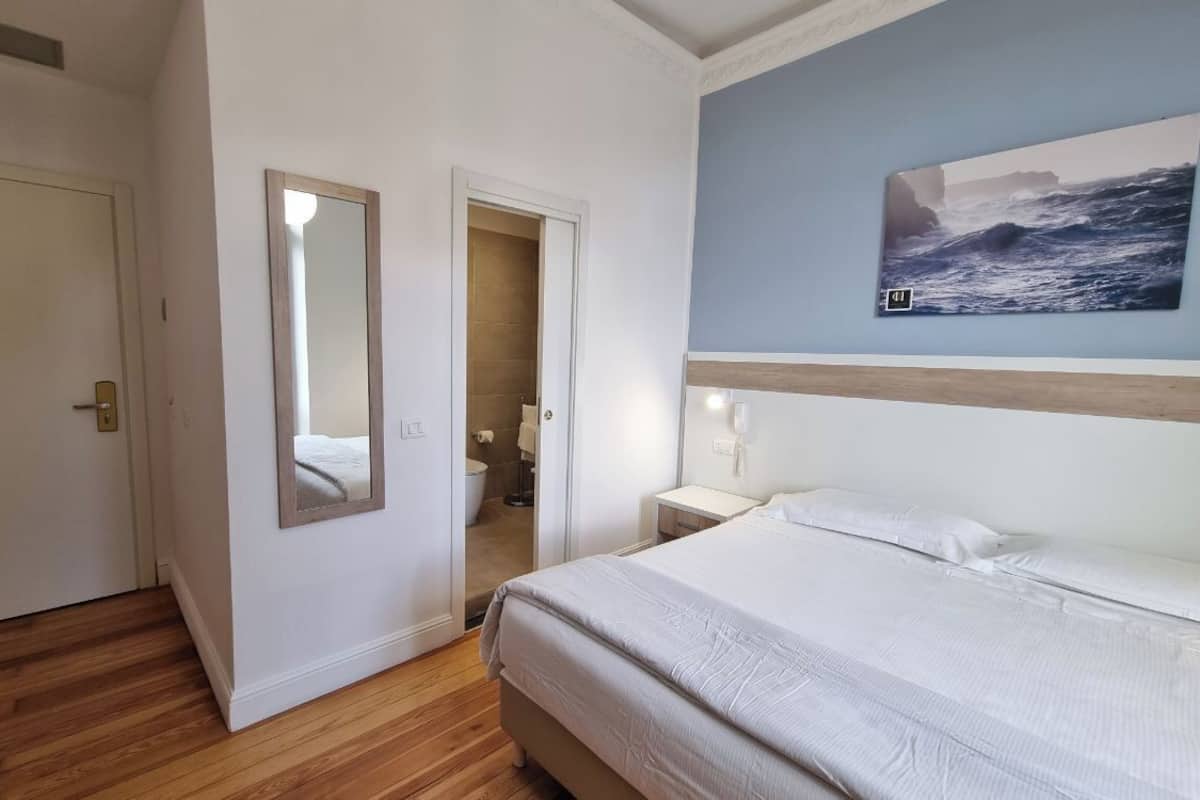 Un dormitorio con cama, espejo, un cuadro y una puerta que da al baño.