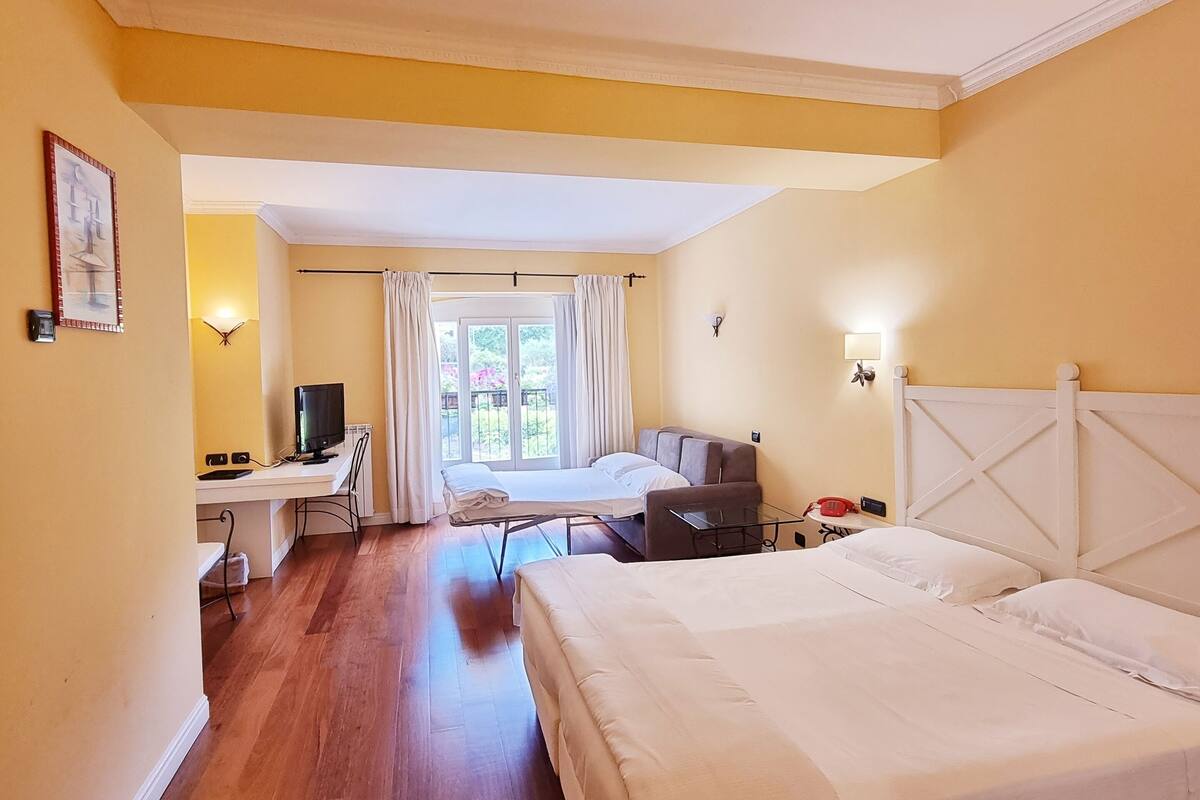 Habitación de hotel con una cama grande, un escritorio con ordenador, una silla y una ventana con cortinas.