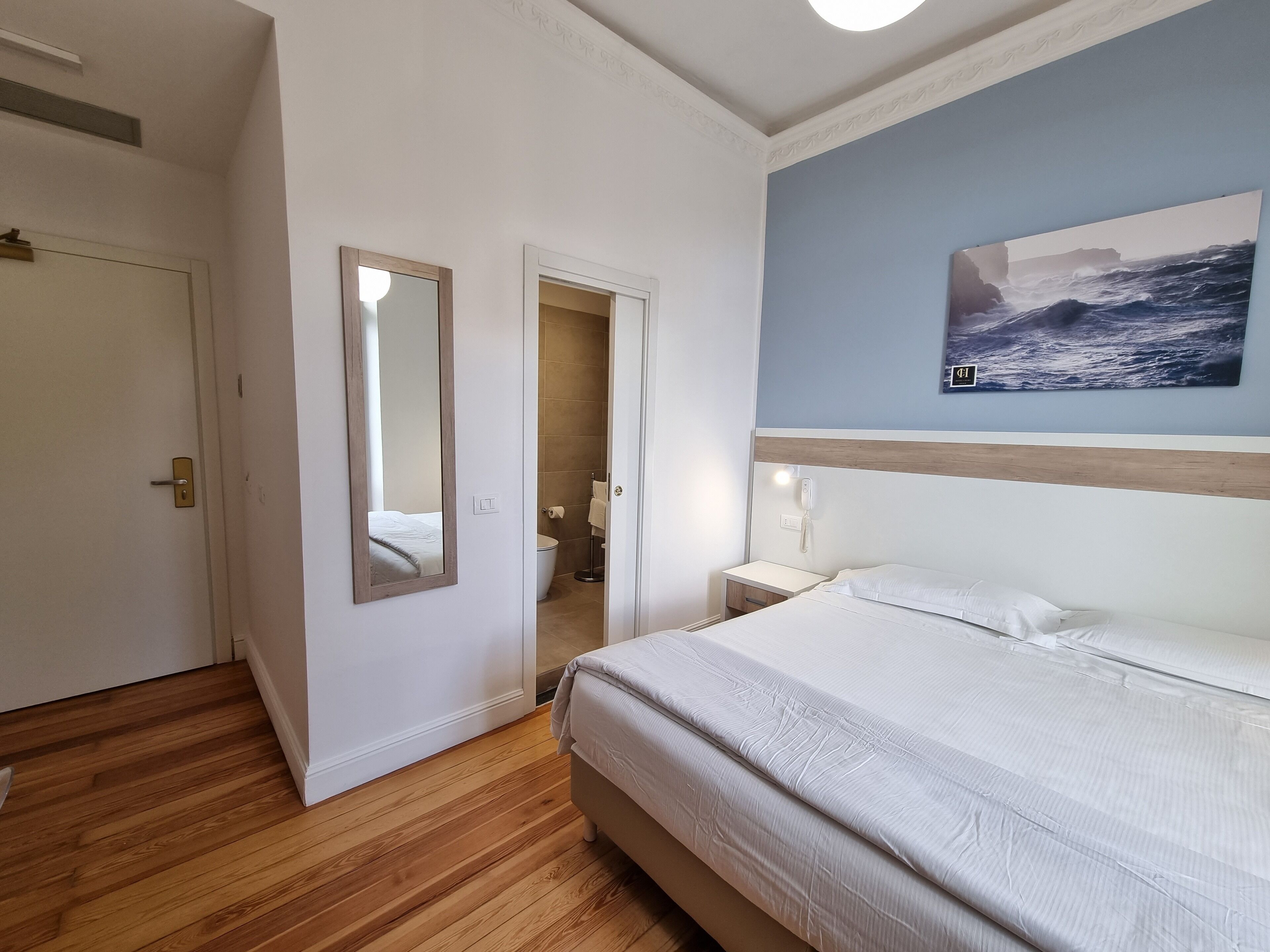 Een hotelkamer met een bed, een badkamer en een schilderij van de oceaan aan de muur.