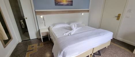 Habitación de hotel con cama, mesita de noche, teléfono en la pared, una puerta y suelo con diseño.