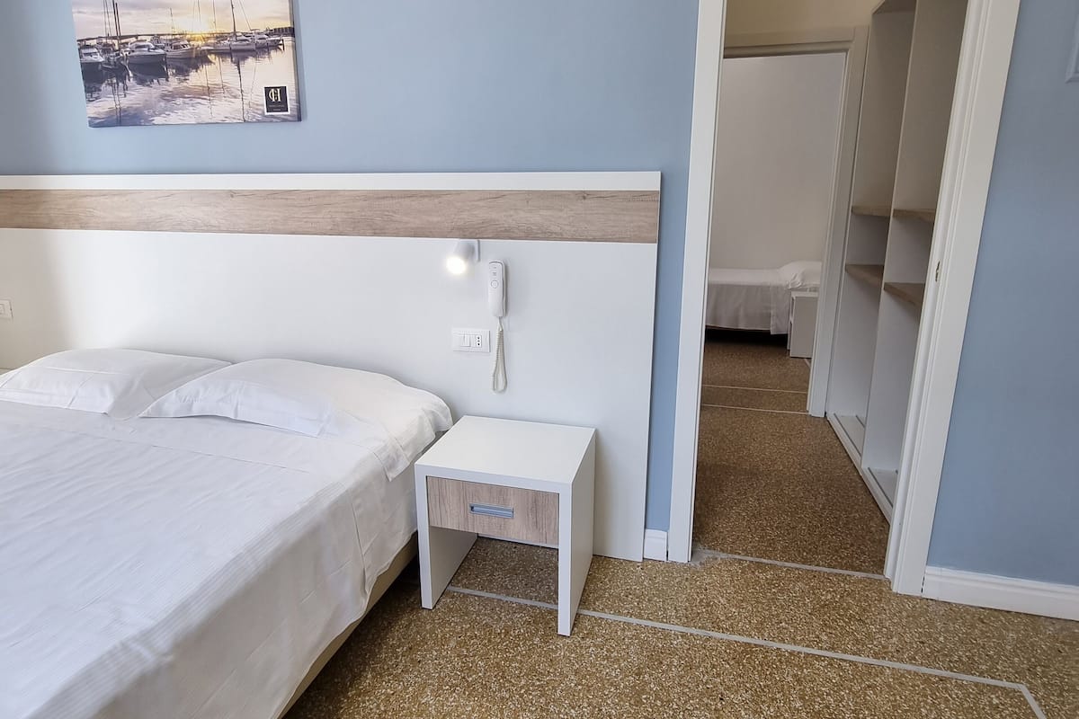 Un dormitorio con cama, mesita de noche e imagen colgada en la pared.