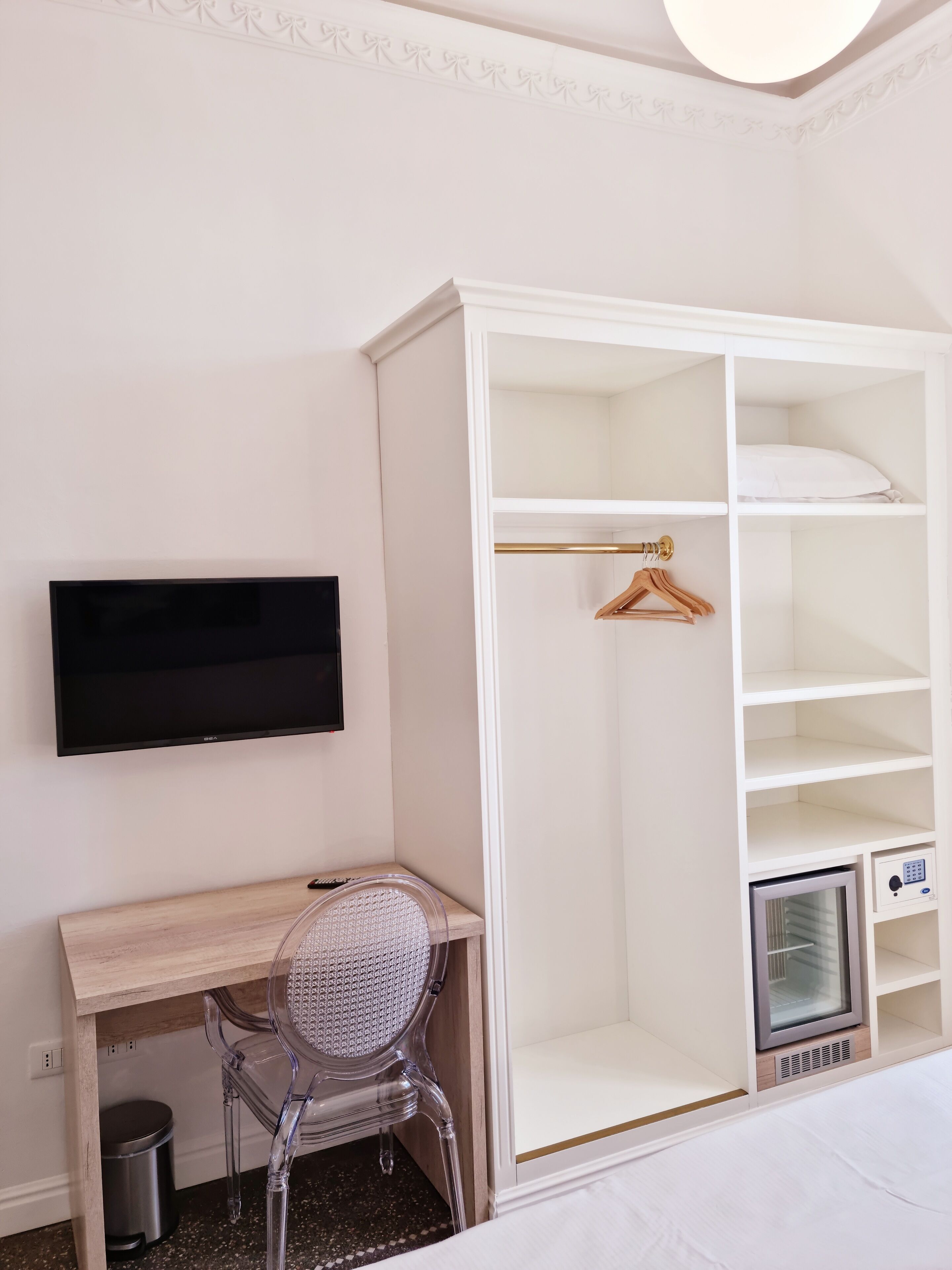 Een slaapkamer met een witte inbouwkast, bureau, stoel, televisie en een minibar.