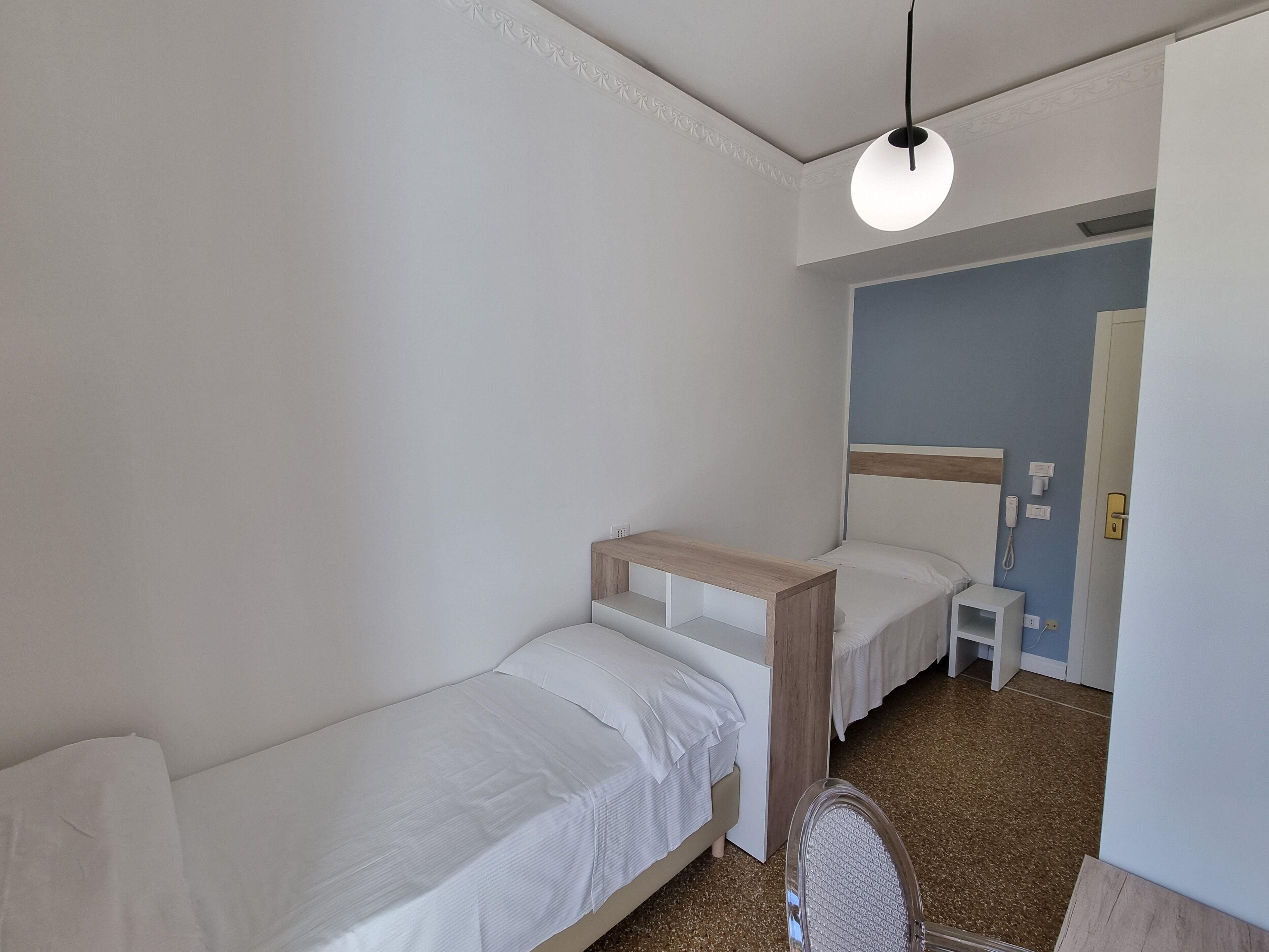 A small, clean room with two single beds, a wooden nightstand, a small table, and a ceiling light.