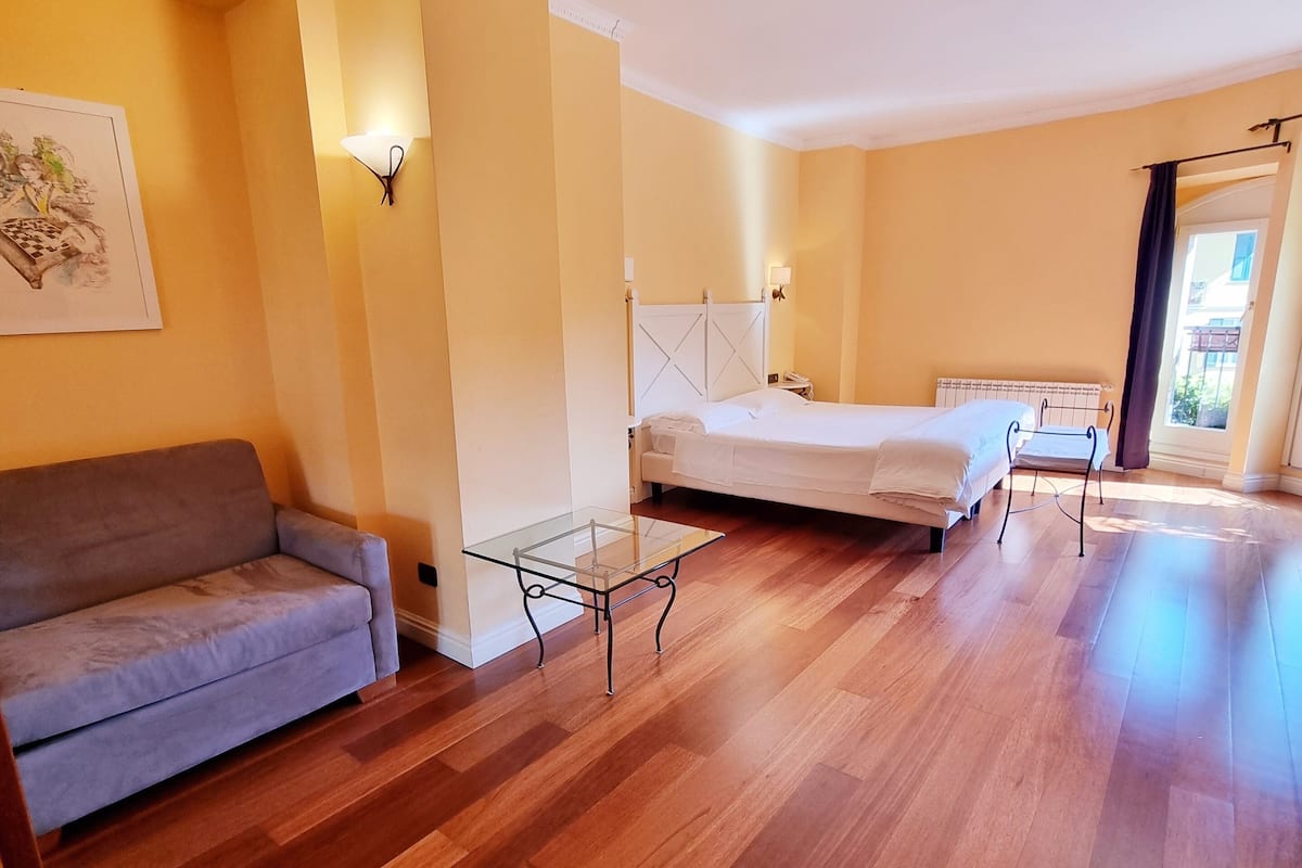 Habitación de hotel con sofá, cama, mesita de vidrio y mesita de noche.