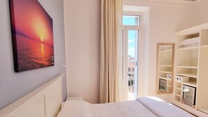Une chambre d’hôtel avec un lit, un tableau représentant un coucher de soleil, une fenêtre avec des rideaux et des étagères intégrées.