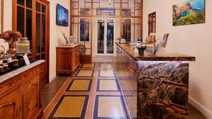 Un hall d’hôtel avec un sol à motifs, des meubles en bois, un lustre et un comptoir d’accueil.