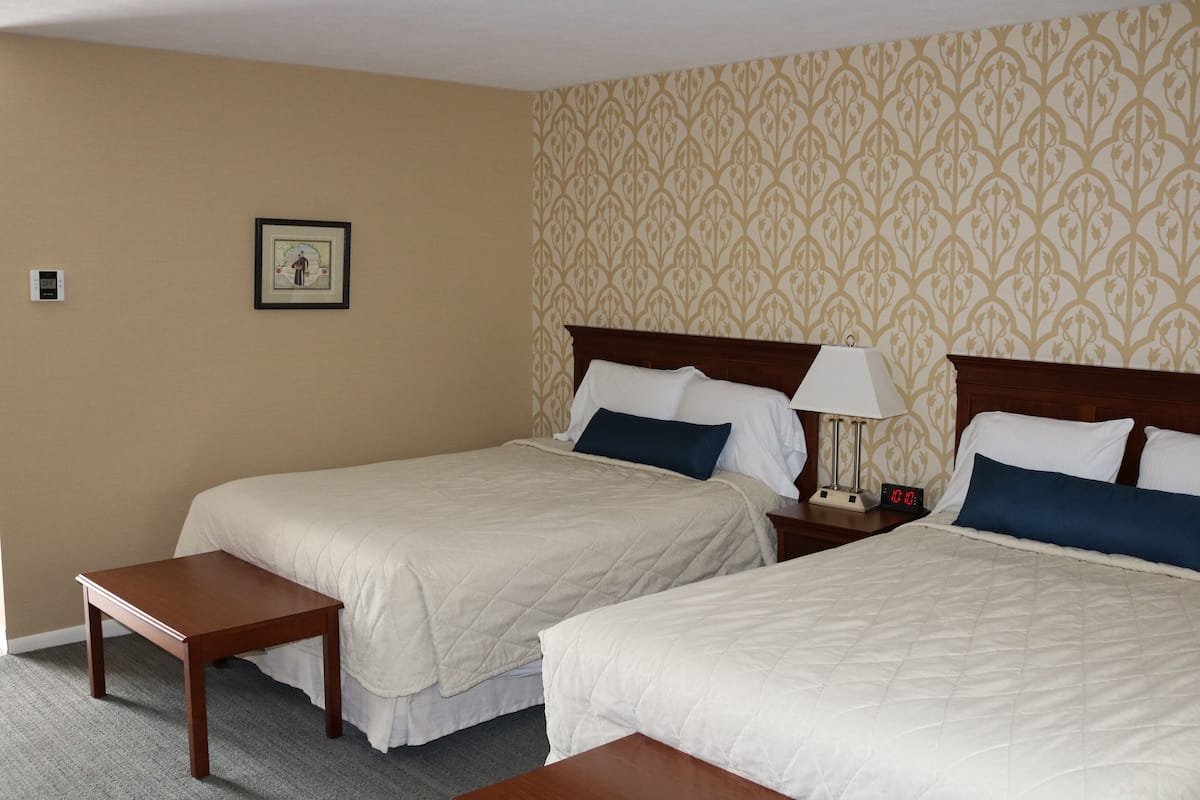 A hotel room with two beds, a nightstand with a lamp, a framed picture on the wall, and a small table.