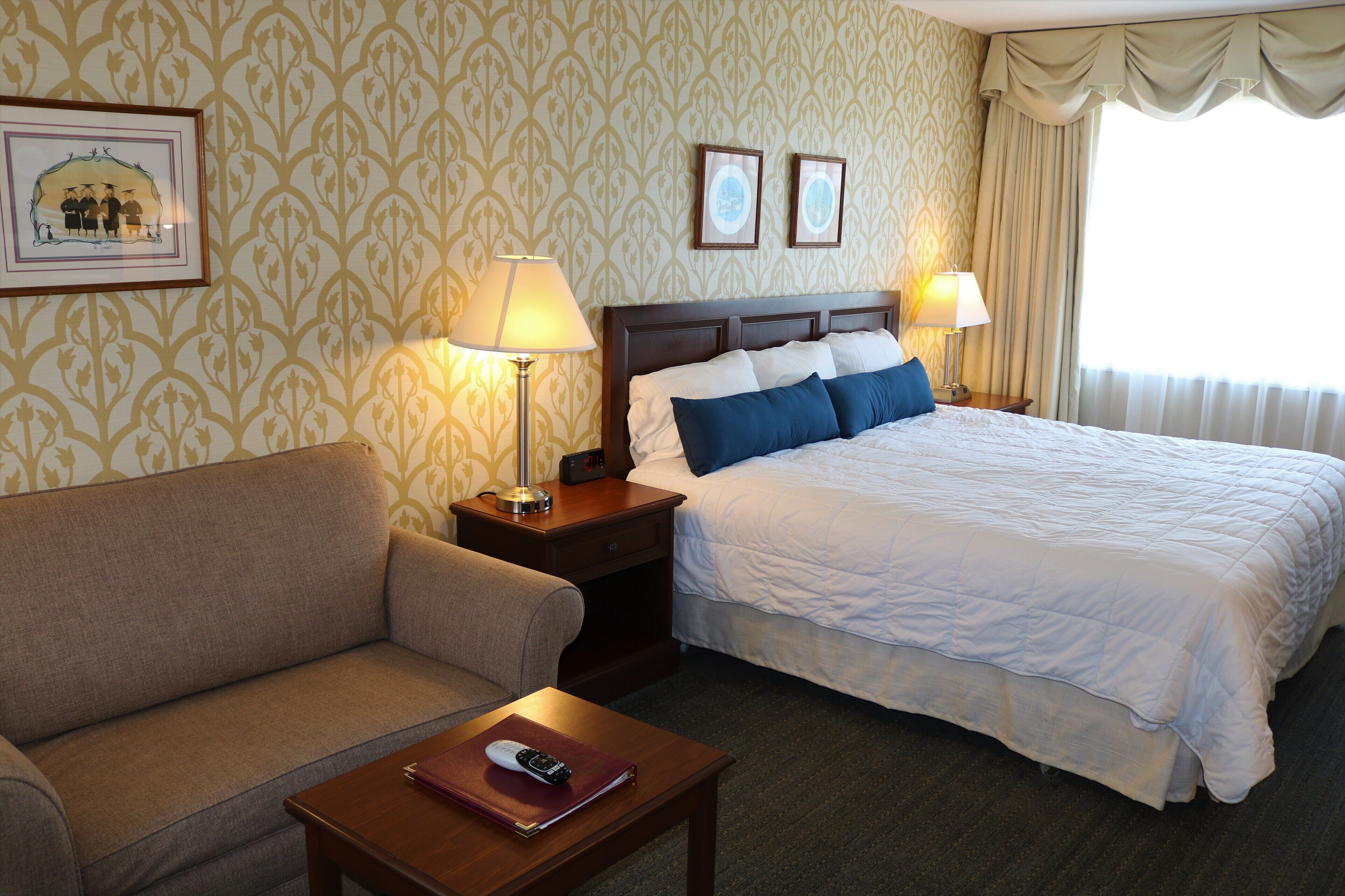 A hotel room with a bed, a sofa, a nightstand, and a lamp.