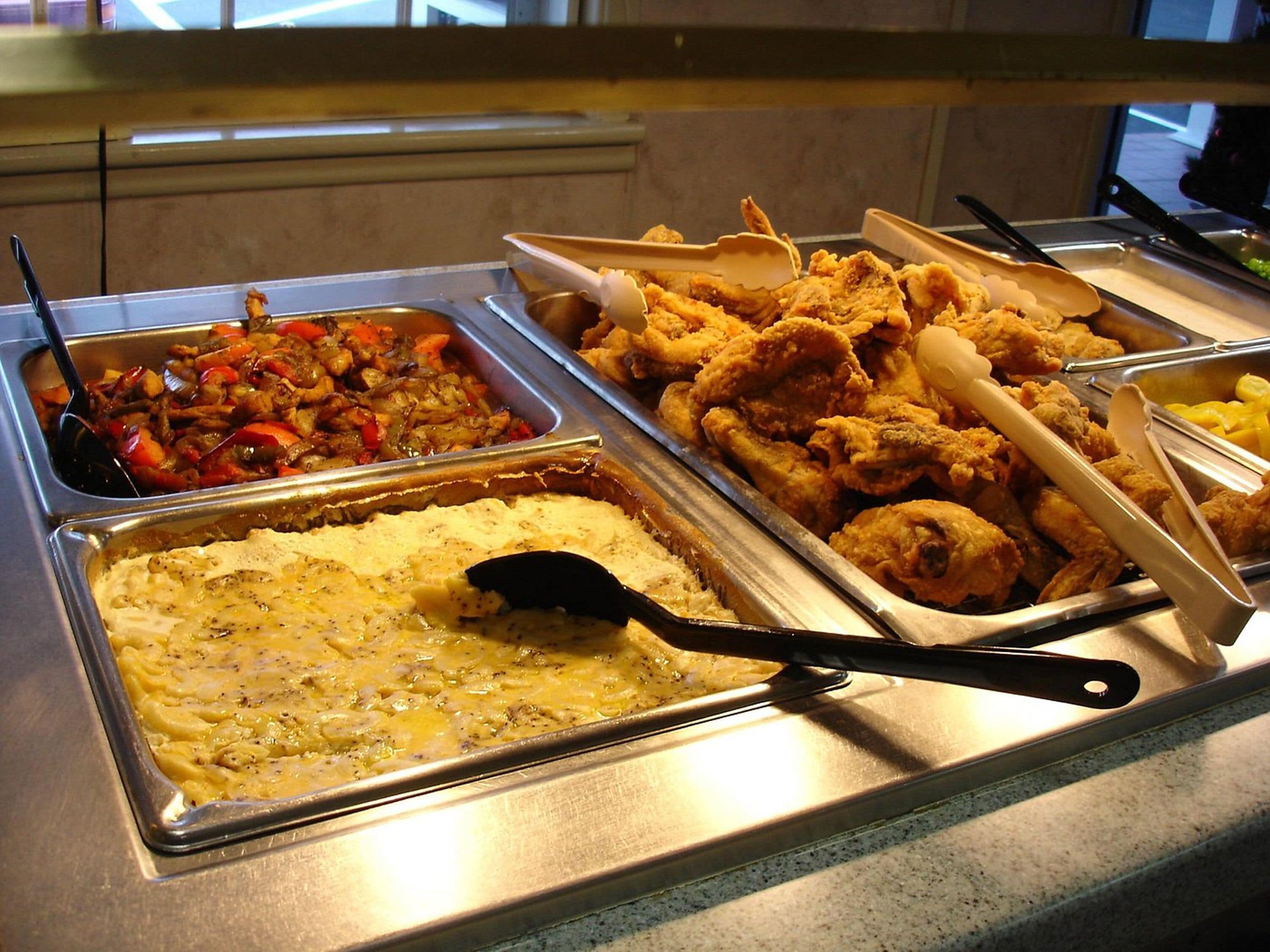 Un buffet proposant divers plats, notamment du poulet frit, des macaronis au fromage et un sauté de légumes.